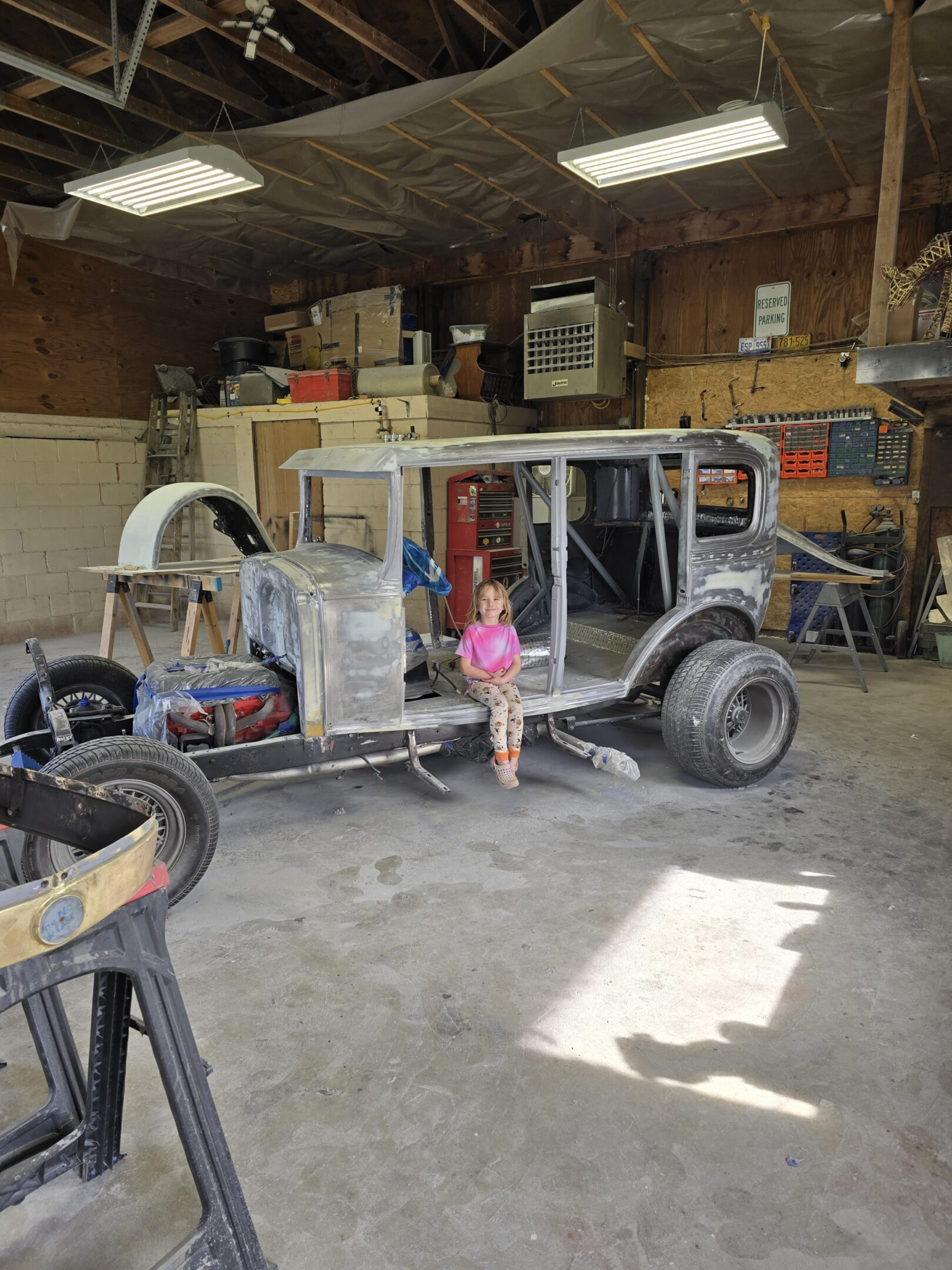 A little girl standing in front of an old car.